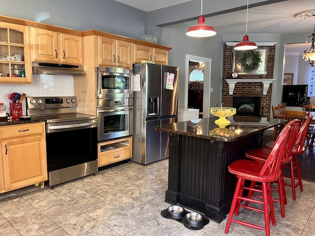 kitchen with a breakfast bar, appliances with stainless steel finishes, a center island, dark stone countertops, and a fireplace