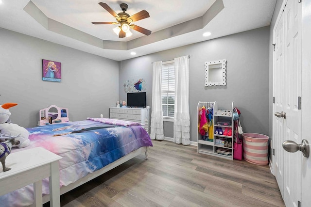 bedroom with ceiling fan, hardwood / wood-style flooring, a raised ceiling, and a closet