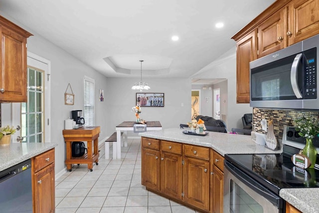 kitchen with light tile patterned flooring, a raised ceiling, hanging light fixtures, stainless steel appliances, and an inviting chandelier