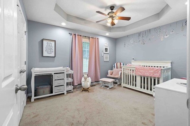 bedroom featuring ceiling fan, a nursery area, a raised ceiling, and light carpet