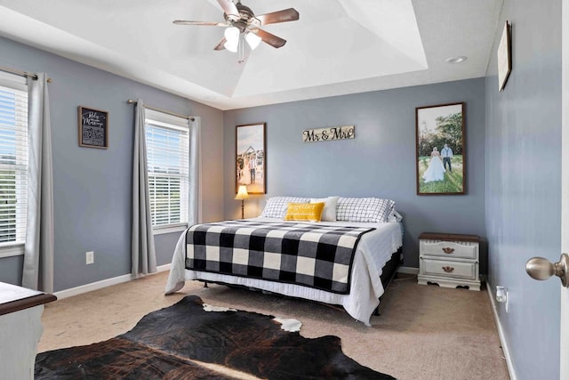 carpeted bedroom with ceiling fan, a tray ceiling, and multiple windows