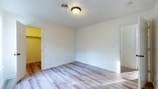 unfurnished bedroom featuring a textured ceiling, a closet, a spacious closet, and light hardwood / wood-style flooring