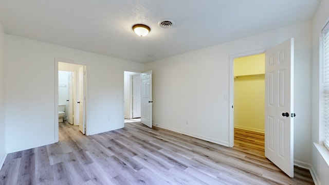 unfurnished bedroom featuring a closet, light hardwood / wood-style floors, a textured ceiling, connected bathroom, and a walk in closet