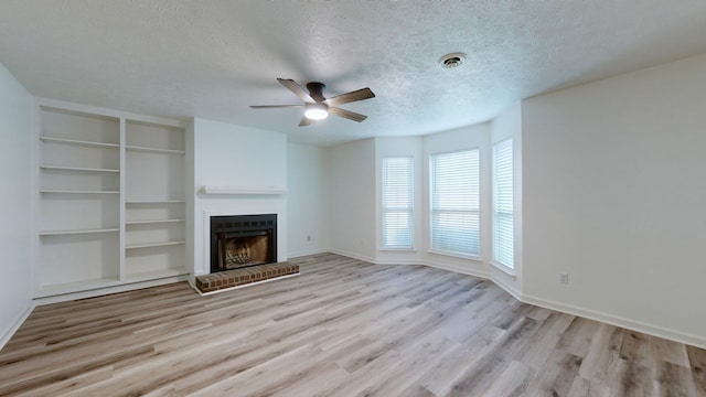 unfurnished living room featuring a brick fireplace, light hardwood / wood-style floors, ceiling fan, and a textured ceiling