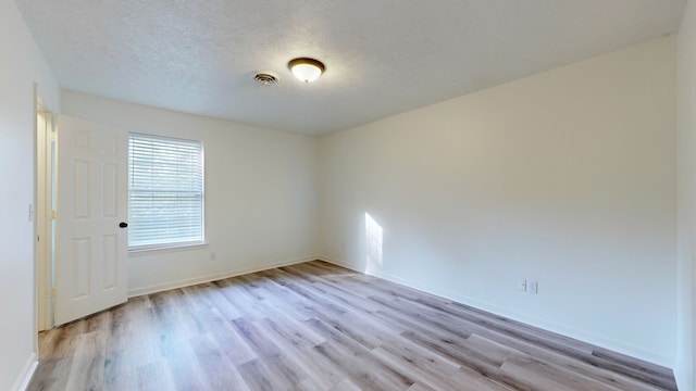 spare room featuring a textured ceiling and light hardwood / wood-style floors