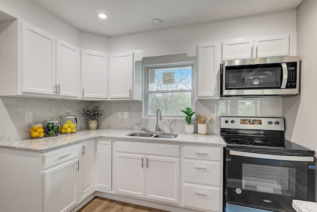 kitchen with appliances with stainless steel finishes, light stone countertops, sink, and white cabinets