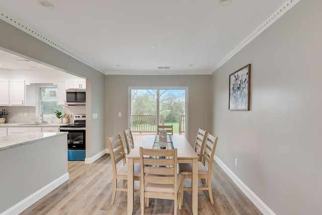 dining area with light hardwood / wood-style flooring, ornamental molding, and a healthy amount of sunlight