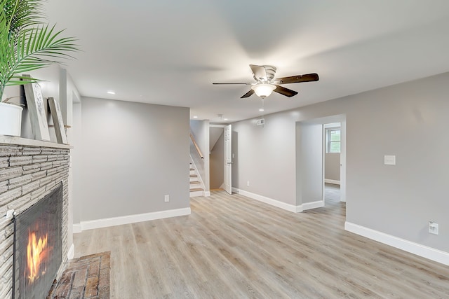 unfurnished living room with light hardwood / wood-style floors, a stone fireplace, and ceiling fan