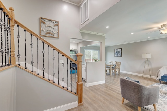 stairway featuring wood-type flooring, ornamental molding, and ceiling fan