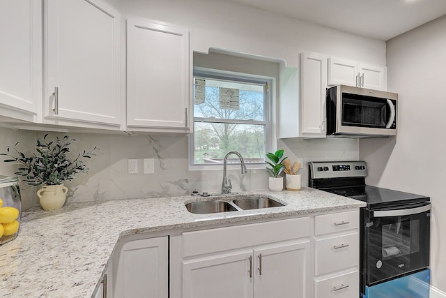 kitchen featuring appliances with stainless steel finishes, decorative backsplash, white cabinetry, light stone countertops, and sink