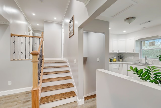 stairs featuring hardwood / wood-style floors, ornamental molding, and sink