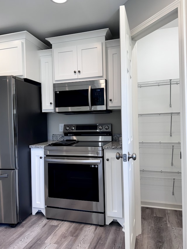 kitchen with light stone countertops, appliances with stainless steel finishes, light wood-type flooring, and white cabinetry