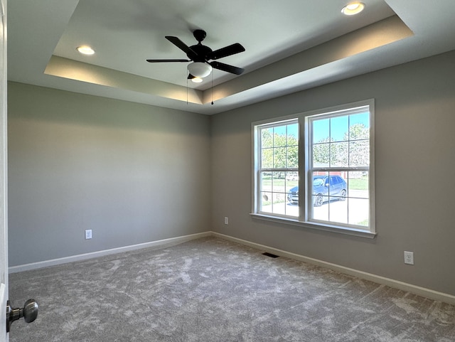 carpeted empty room with a raised ceiling and ceiling fan