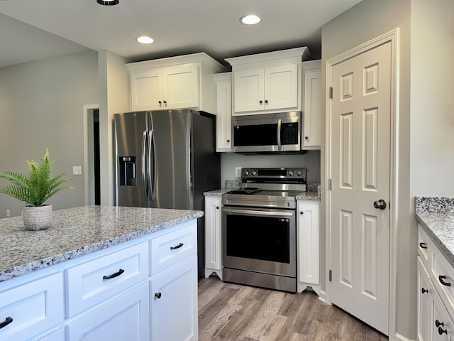 kitchen with white cabinets, appliances with stainless steel finishes, light stone countertops, and light hardwood / wood-style flooring