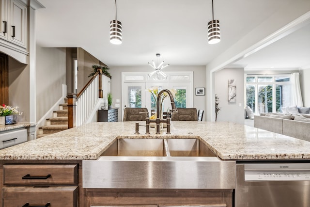 kitchen with hanging light fixtures, stainless steel dishwasher, and light stone counters