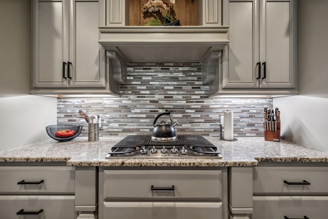 kitchen with stainless steel gas stovetop, light stone counters, gray cabinets, and tasteful backsplash