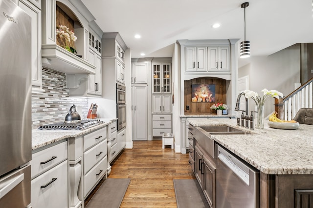 kitchen with dark wood-type flooring, light stone countertops, stainless steel appliances, decorative light fixtures, and sink