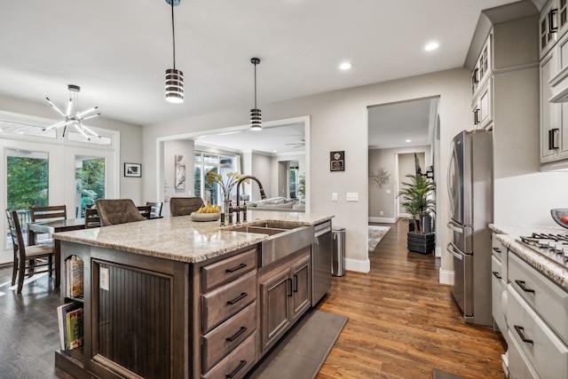 kitchen with sink, decorative light fixtures, appliances with stainless steel finishes, light stone countertops, and dark hardwood / wood-style flooring