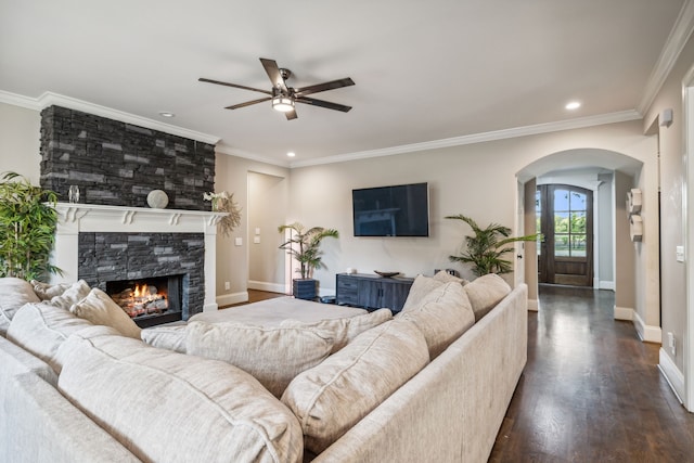 living room featuring ceiling fan, ornamental molding, a tiled fireplace, and dark hardwood / wood-style flooring