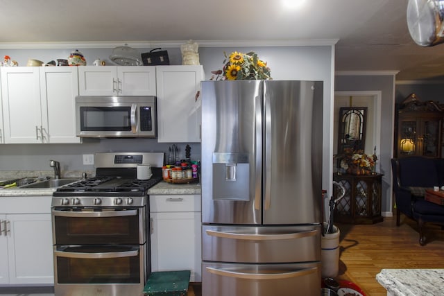 kitchen featuring wood-type flooring, crown molding, stainless steel appliances, and white cabinets