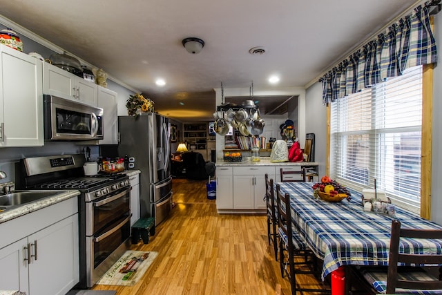 kitchen with white cabinets, sink, light hardwood / wood-style flooring, appliances with stainless steel finishes, and crown molding