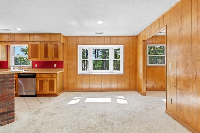 kitchen with a textured ceiling, wooden walls, dishwasher, and light carpet