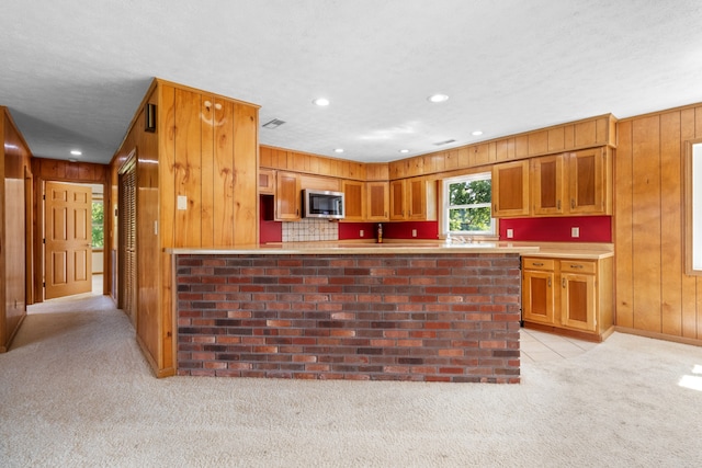 kitchen with light carpet, wooden walls, kitchen peninsula, and a textured ceiling