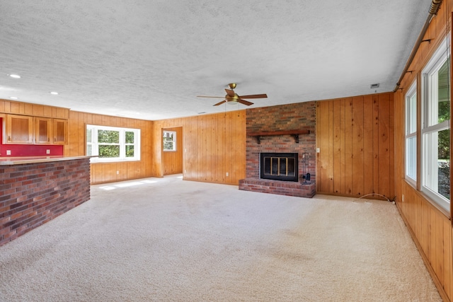 unfurnished living room with wood walls, a textured ceiling, light colored carpet, and a fireplace