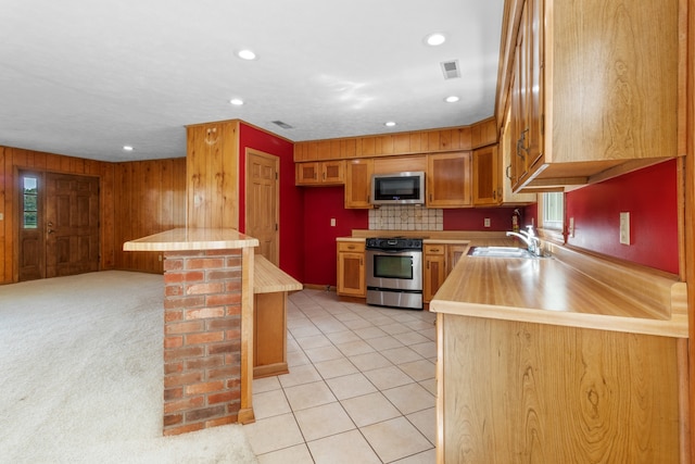 kitchen with tasteful backsplash, wood walls, stainless steel appliances, sink, and light colored carpet