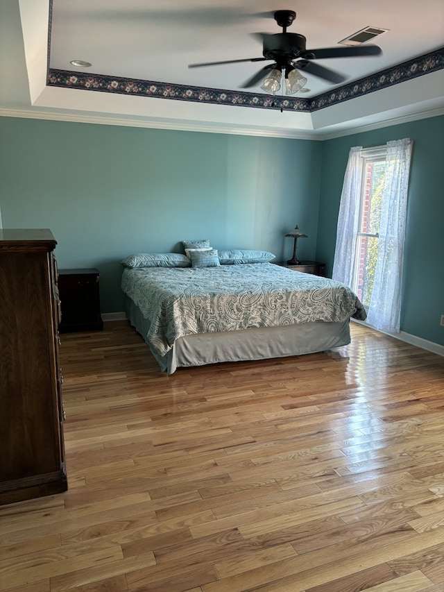 bedroom with light wood-type flooring, a raised ceiling, ornamental molding, and ceiling fan