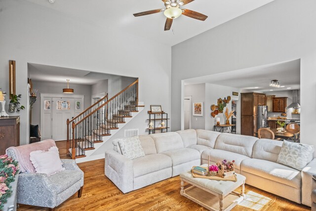 living room with light wood-type flooring, a high ceiling, and ceiling fan