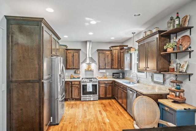 kitchen featuring light hardwood / wood-style floors, stainless steel appliances, decorative light fixtures, sink, and wall chimney range hood