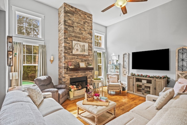 living room featuring light hardwood / wood-style flooring, a high ceiling, ceiling fan, and a stone fireplace