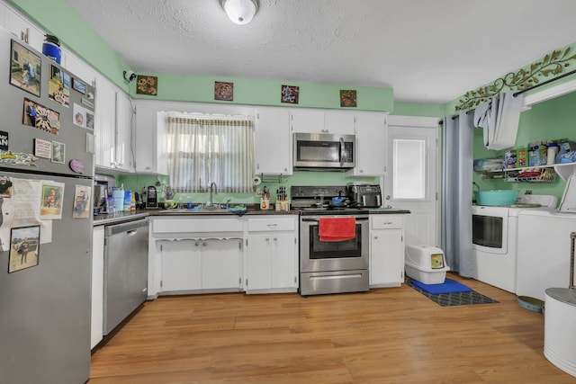 kitchen with light wood-type flooring, sink, washing machine and clothes dryer, white cabinets, and appliances with stainless steel finishes