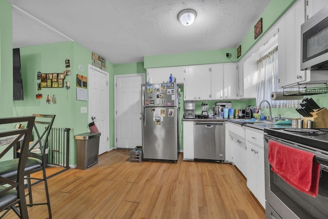 kitchen featuring appliances with stainless steel finishes, light hardwood / wood-style floors, white cabinets, a textured ceiling, and sink