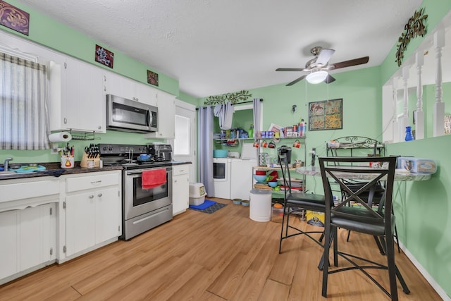 kitchen with ceiling fan, washing machine and clothes dryer, white cabinetry, stainless steel appliances, and light wood-type flooring