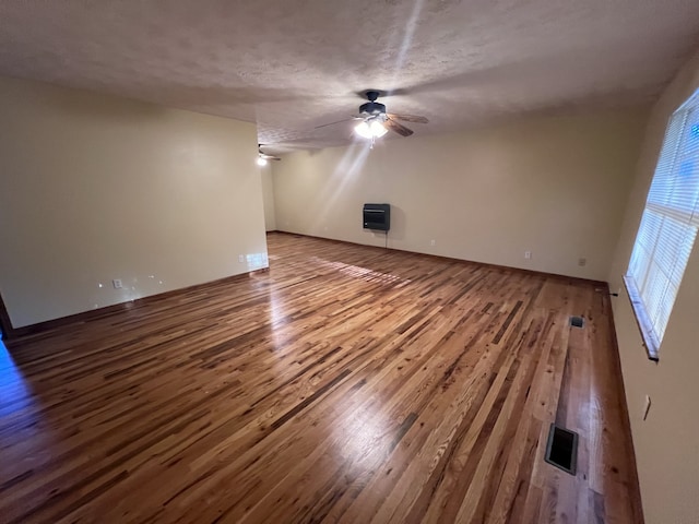 unfurnished living room featuring heating unit, wood-type flooring, a textured ceiling, and ceiling fan