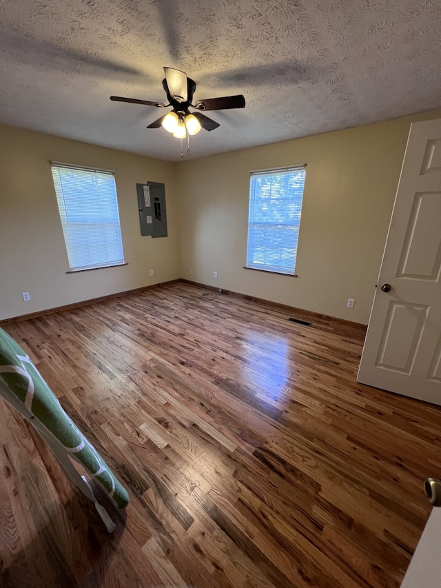 spare room with a textured ceiling, electric panel, ceiling fan, and hardwood / wood-style flooring