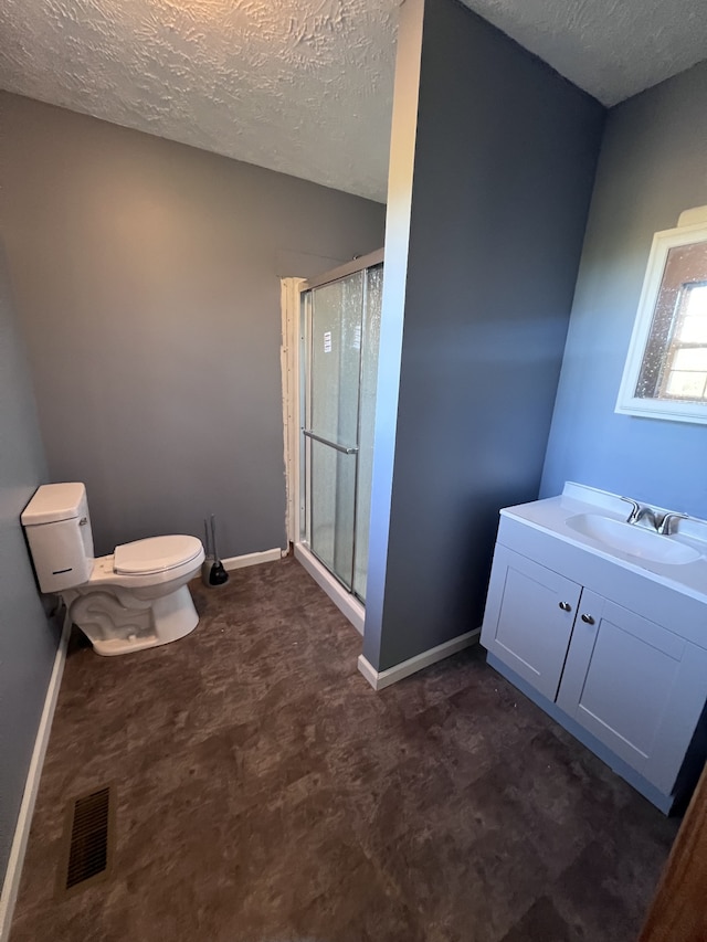 bathroom featuring a textured ceiling, a shower with door, toilet, and vanity