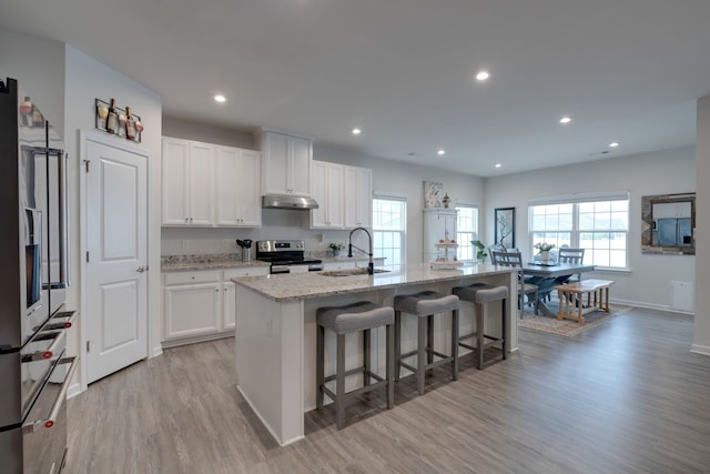 kitchen with a breakfast bar, sink, an island with sink, white cabinets, and electric stove