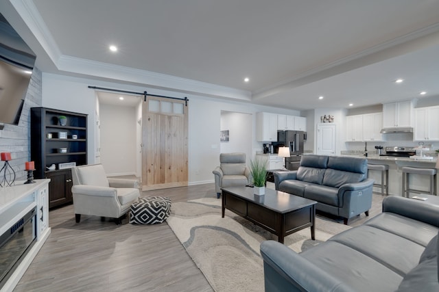 living room featuring light hardwood / wood-style flooring, crown molding, and a barn door