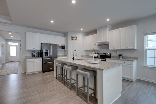 kitchen with stainless steel appliances, white cabinetry, and a center island with sink