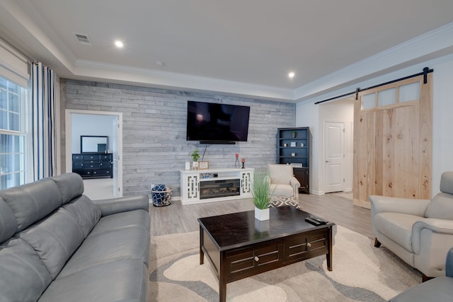 living room with light hardwood / wood-style floors, crown molding, and a barn door