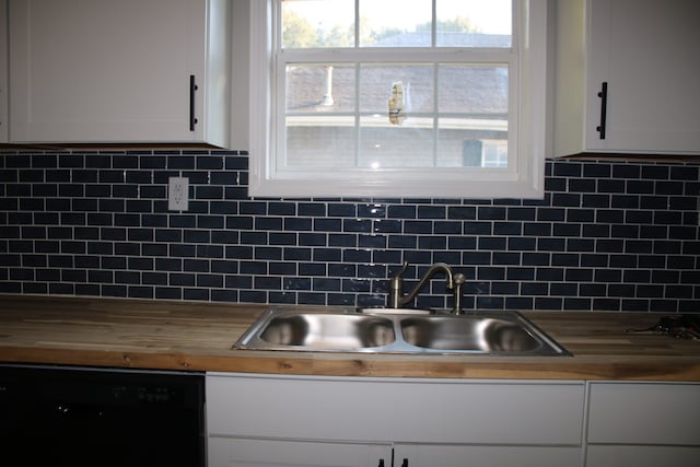 kitchen with sink, backsplash, white cabinetry, black dishwasher, and butcher block counters