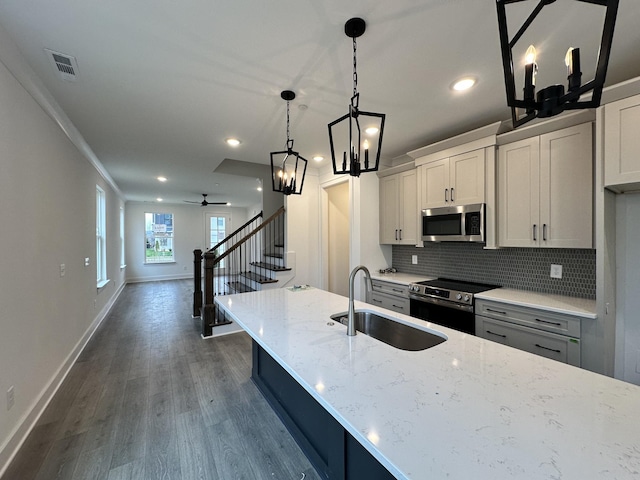 kitchen with light stone countertops, ceiling fan with notable chandelier, stainless steel appliances, and sink