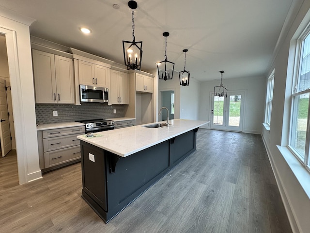 kitchen with a kitchen island with sink, hanging light fixtures, sink, light hardwood / wood-style flooring, and appliances with stainless steel finishes