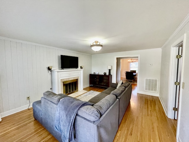 living room featuring a fireplace, crown molding, light wood-type flooring, a notable chandelier, and wood walls