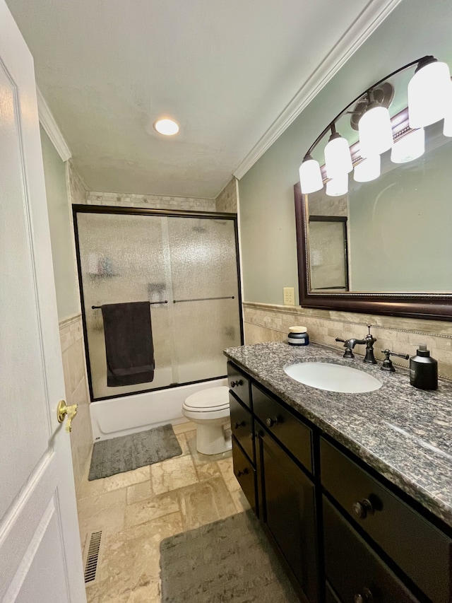 full bathroom with toilet, tile walls, ornamental molding, shower / bath combination with glass door, and vanity