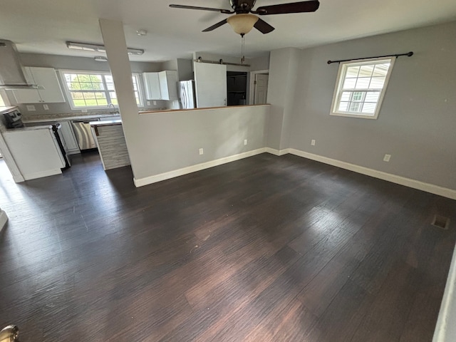 unfurnished living room with a barn door, dark hardwood / wood-style flooring, ceiling fan, and a wealth of natural light