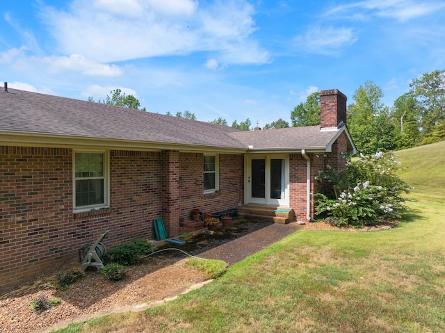exterior space featuring brick siding, a yard, roof with shingles, and a chimney
